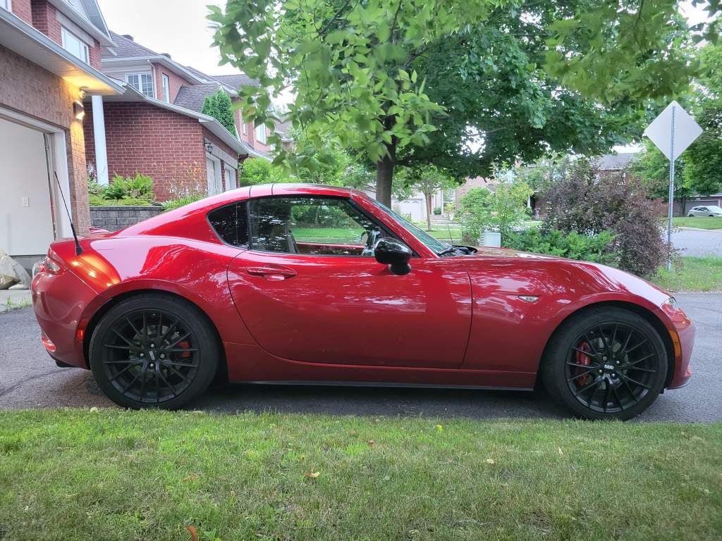 Red sports car parked on driveway, side view.