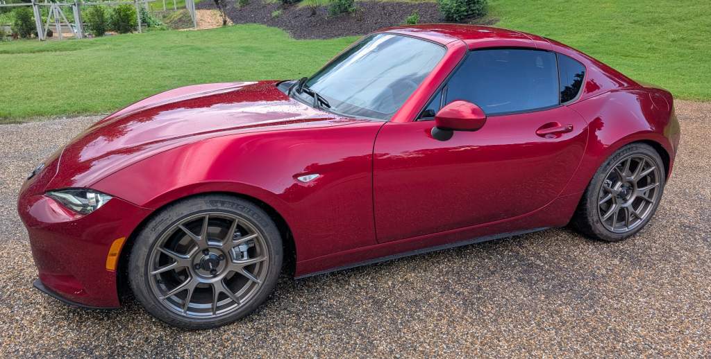 Red sports car parked on gravel driveway.